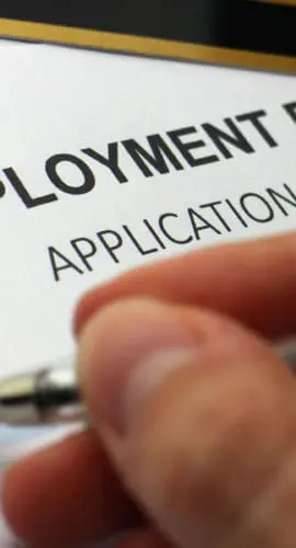 A person is filling out an unemployment benefits application form with a pen.