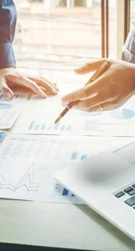 Professionals are engaged in a discussion over documents with charts and data, with a laptop and other office materials on the table.