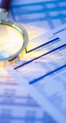A magnifying glass lies on top of financial documents next to a calculator, suggesting a detailed financial analysis or audit.