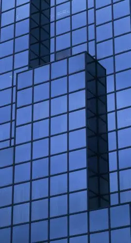 A close-up of a blue glass-clad building facade showing the pattern of windows and a protruding architectural feature.